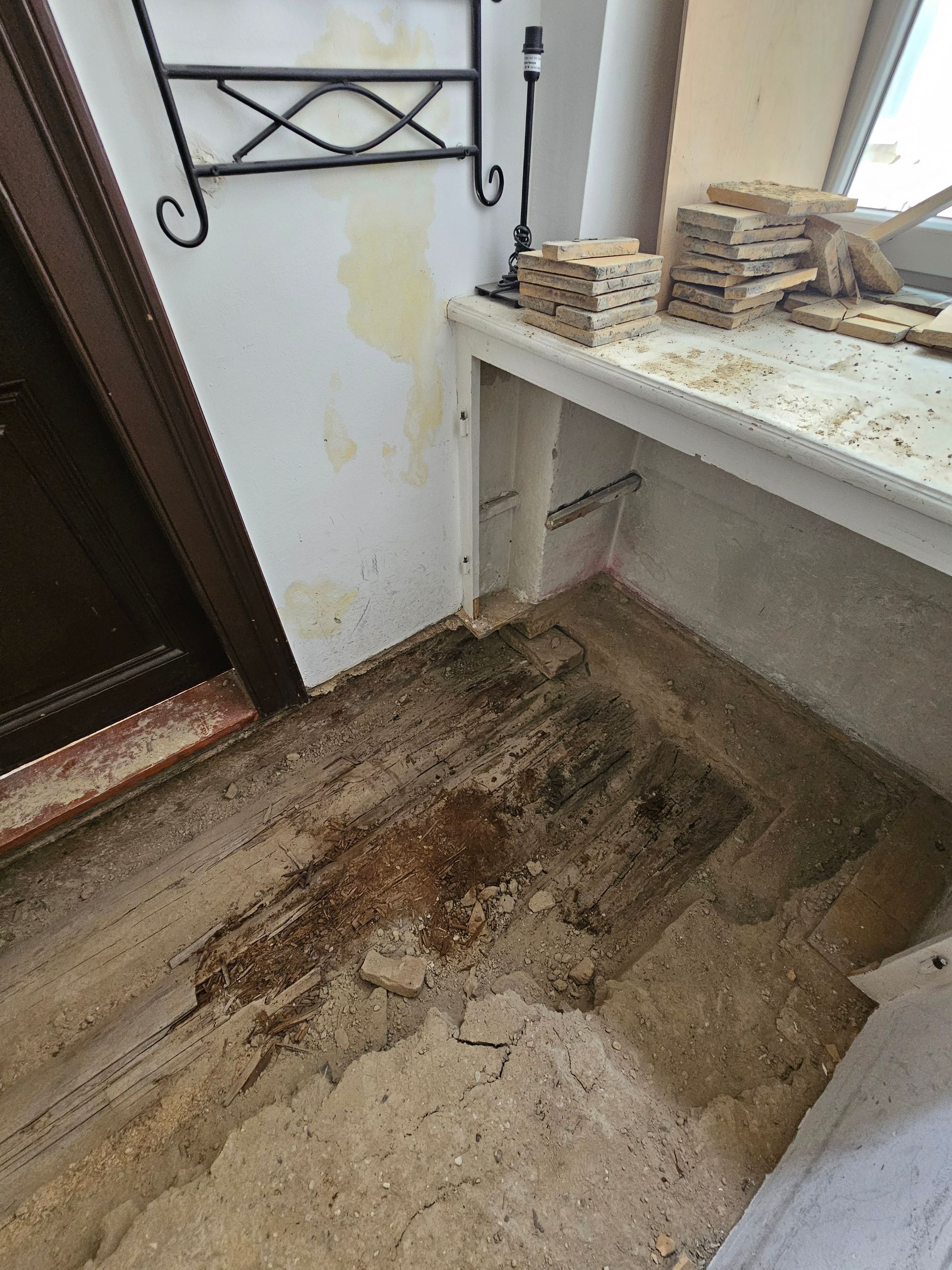 Ein Raum mit einer durch Wasser beschädigten Wand, einer weißen Arbeitsplatte und einem unebenen, mit Bauschutt bedeckten Boden in einem Baustellen- oder Reparaturbereich.