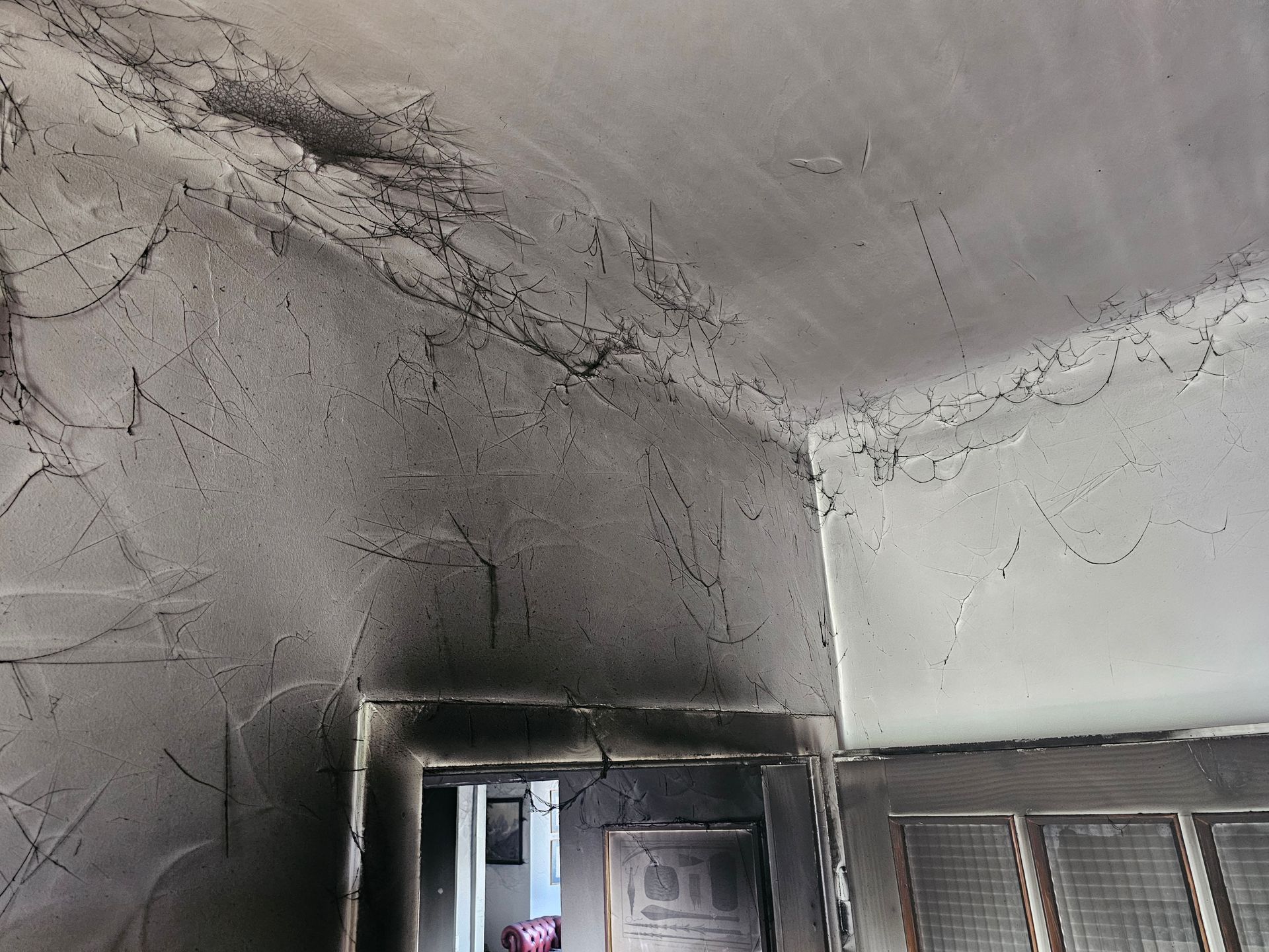 Eine Zimmerecke mit deutlichen Rauch- und Brandschäden; Decke und obere Wände sind mit dunklem Ruß bedeckt.