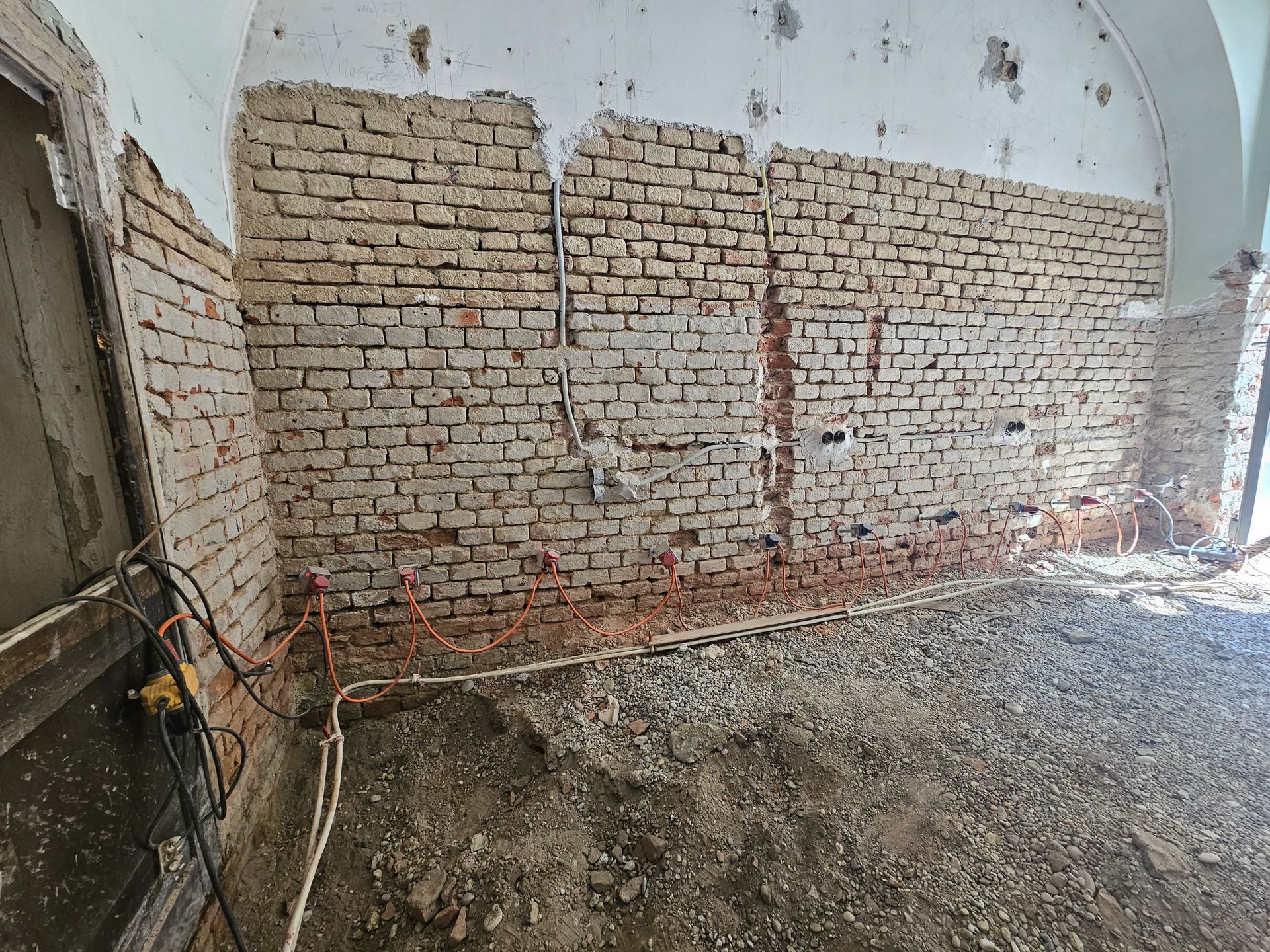 Innenansicht eines Raumes, der gerade renoviert wird; zu sehen sind freiliegende Ziegelwände, elektrische Leitungen und ein mit Bauschutt bedeckter Boden.