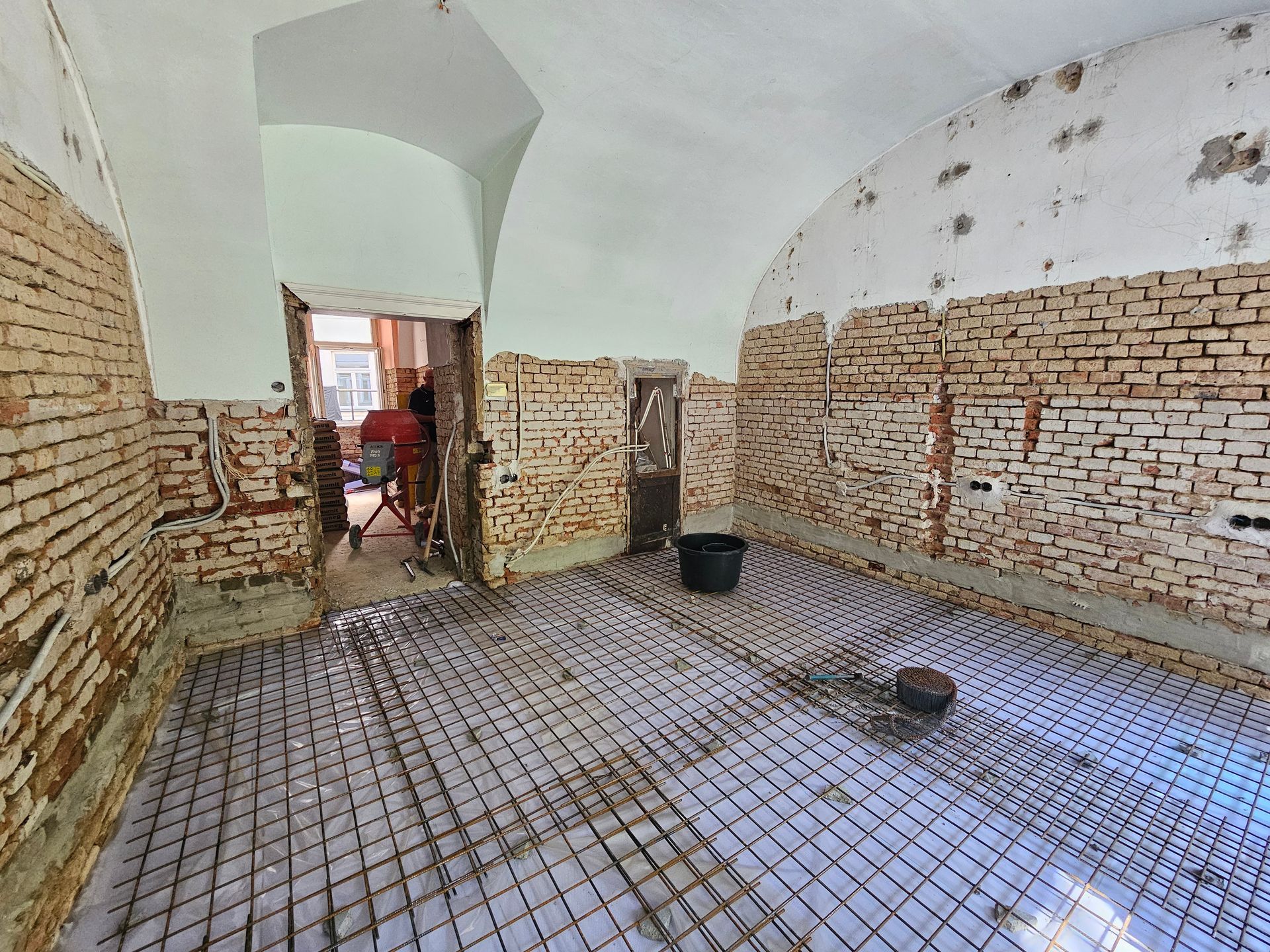 Ein im Bau befindlicher Raum mit freiliegenden Ziegelwänden, einer gewölbten Decke und einer installierten gitterförmigen Fußbodenheizung.