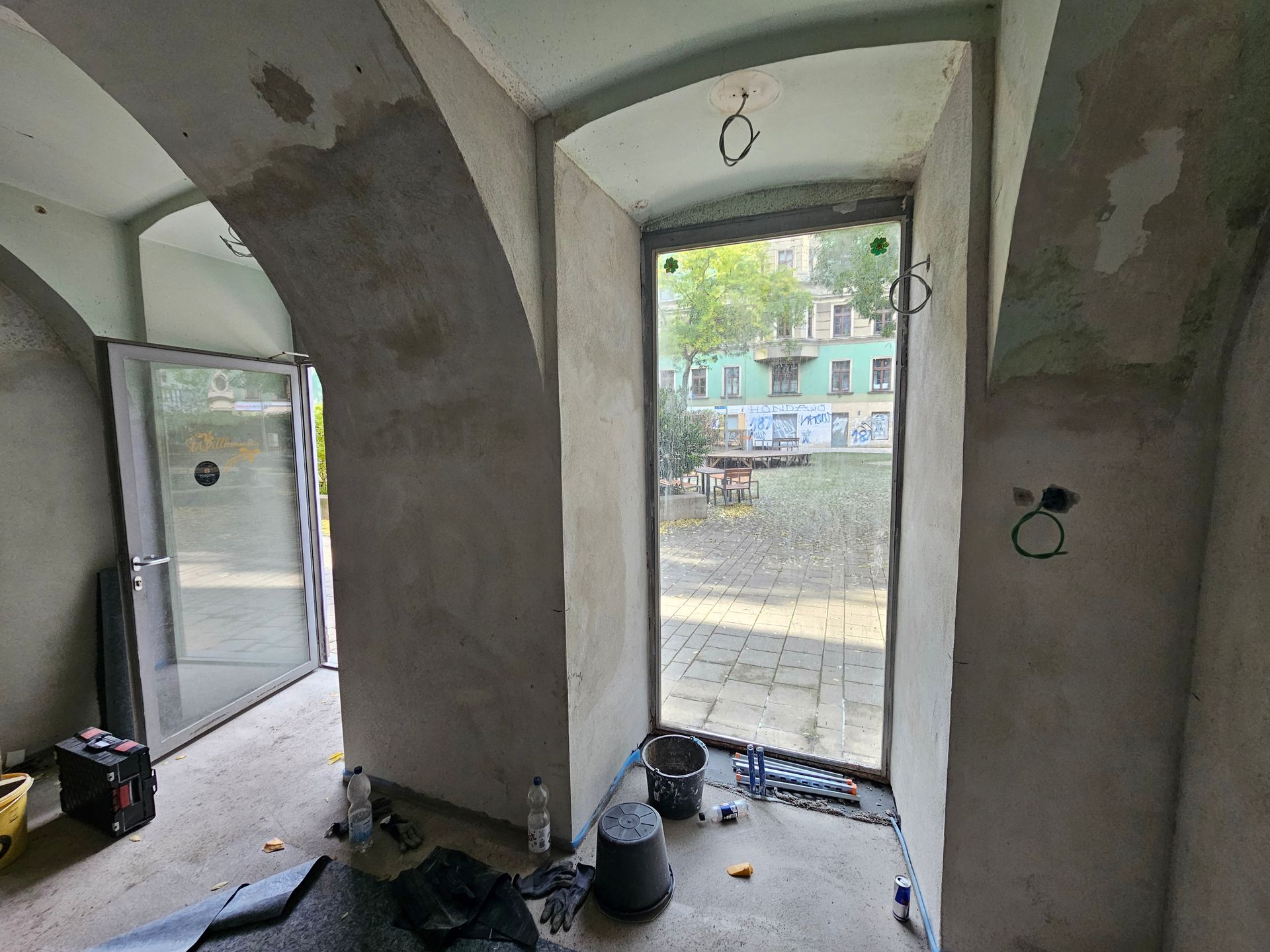 Innenansicht einer Baustelle für einen Bogeneingang mit unverputzten Wänden und Blick auf einen gepflasterten Außenhof.