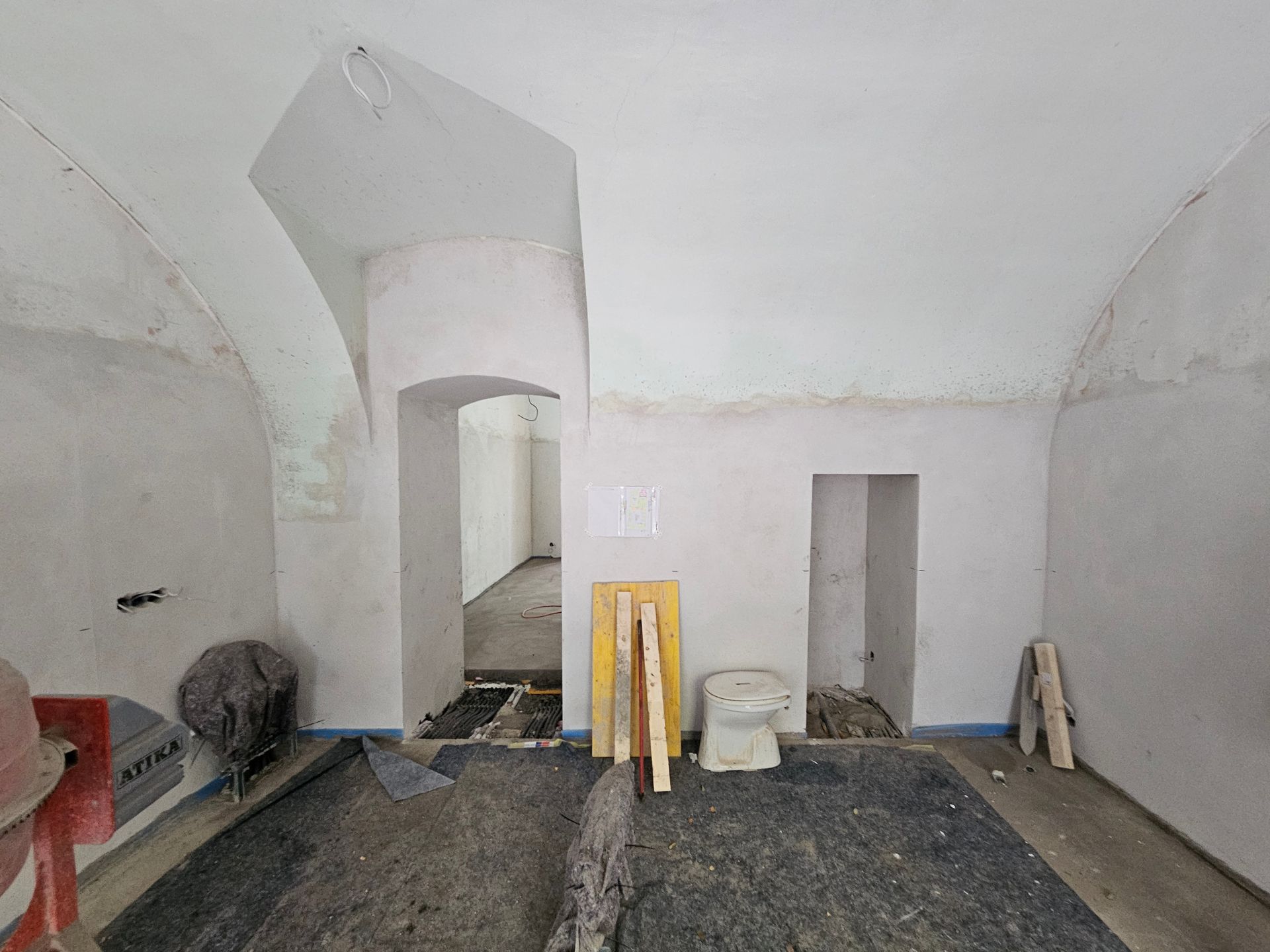 Ein Raum im Umbau mit weißen Gewölbedecken, unfertigen Wänden, zwei Bogentüren und Baumaterialien.
