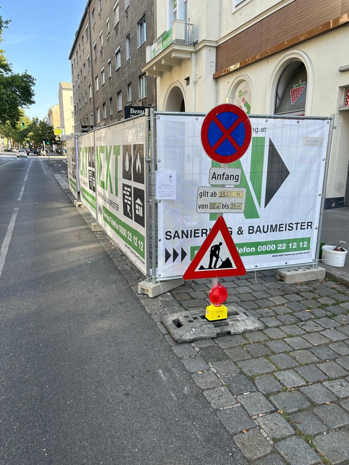 Baustelle auf einem städtischen Gehweg mit einem provisorischen Zaun, einem Parkverbotsschild und einem Warnschild für Straßenarbeiten.