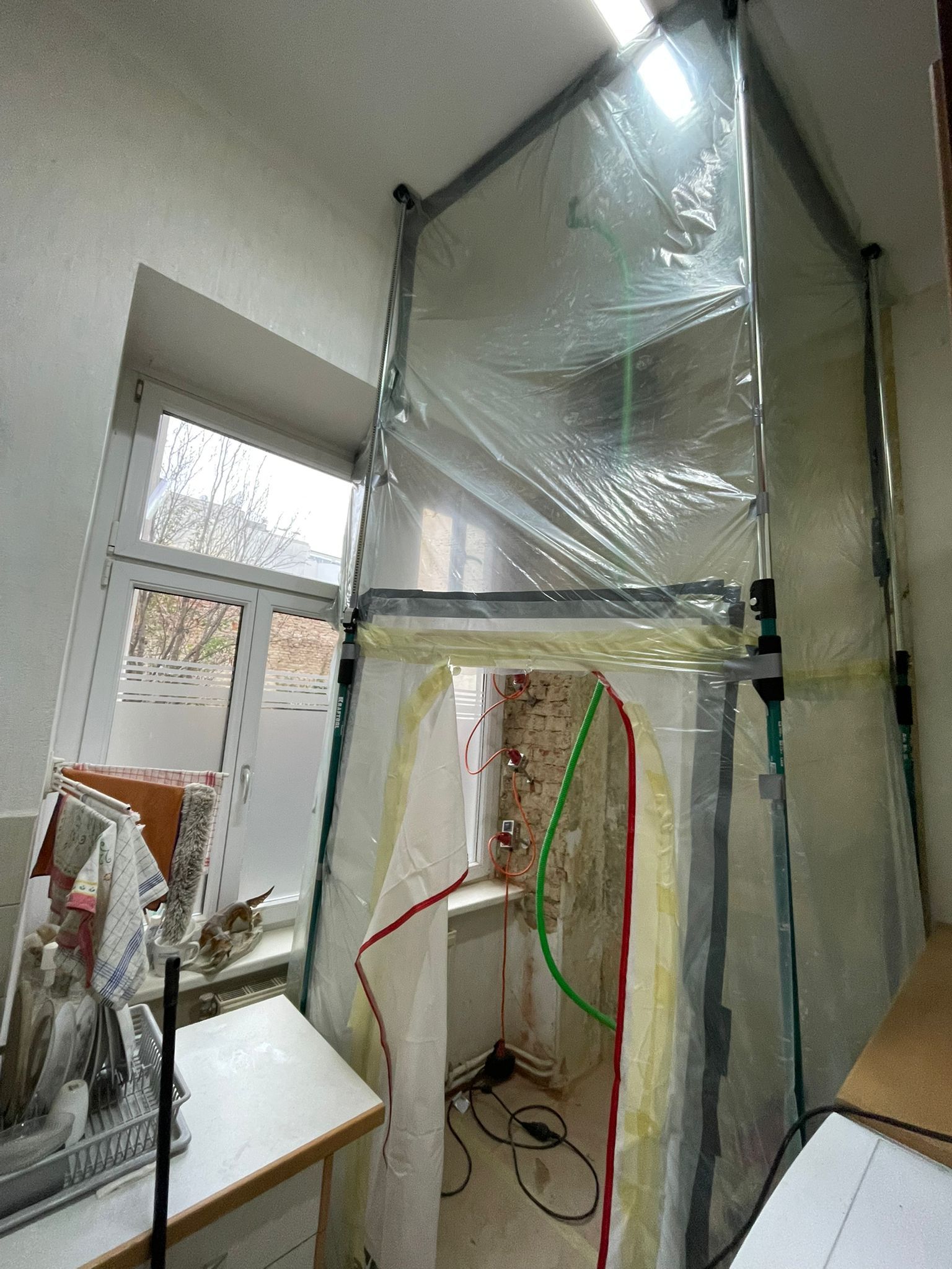 In einem Raum neben einem Fenster wurde eine provisorische Kunststoff-Schutzkabine für Renovierungsarbeiten aufgebaut.