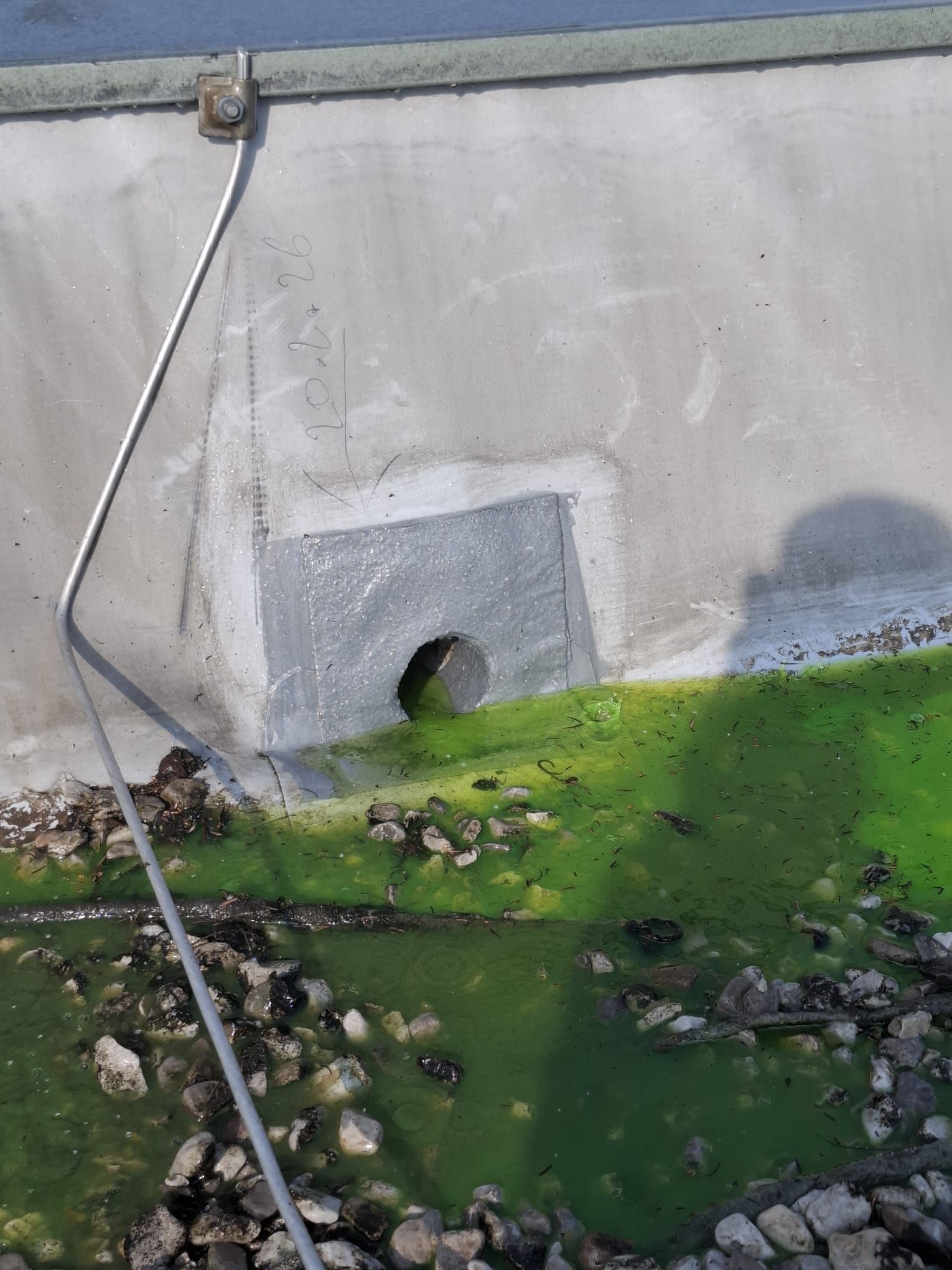 Ein Dachablauf, umgeben von stehendem grünem Wasser, Schutt und Kies.