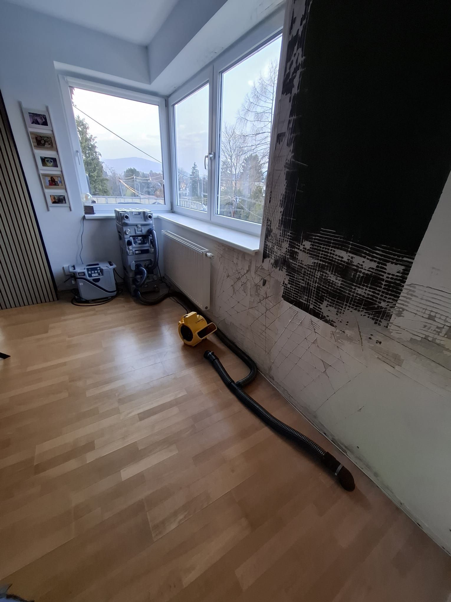 Eine industrielle Trocknungsanlage mit gelbem Ventilator und schwarzem Schlauch steht auf einem Holzboden in einem Raum mit kahlen Wänden.