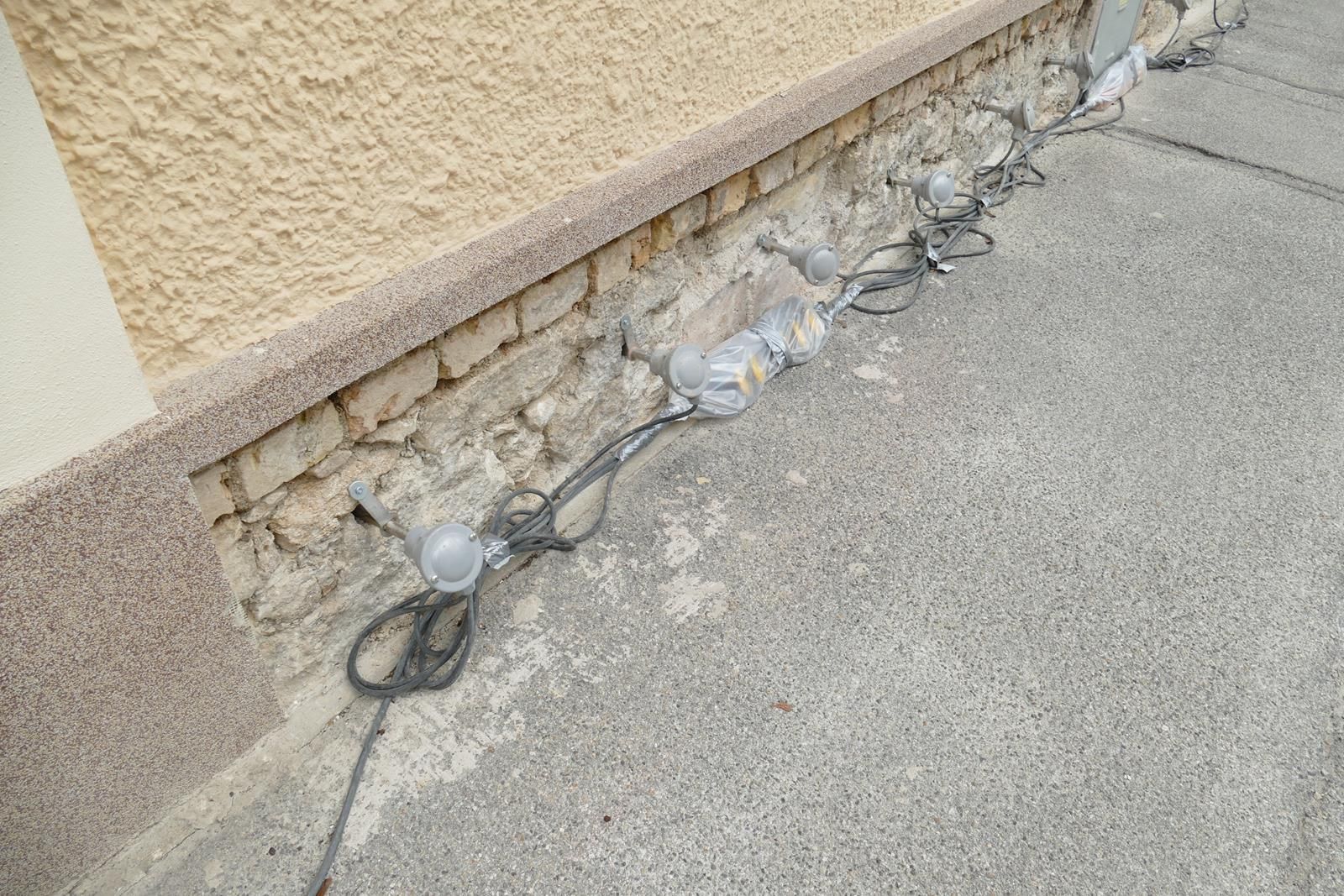Eine Lichterkette für den Außenbereich liegt auf dem Betonboden am Fuße einer strukturierten gelben Wand.