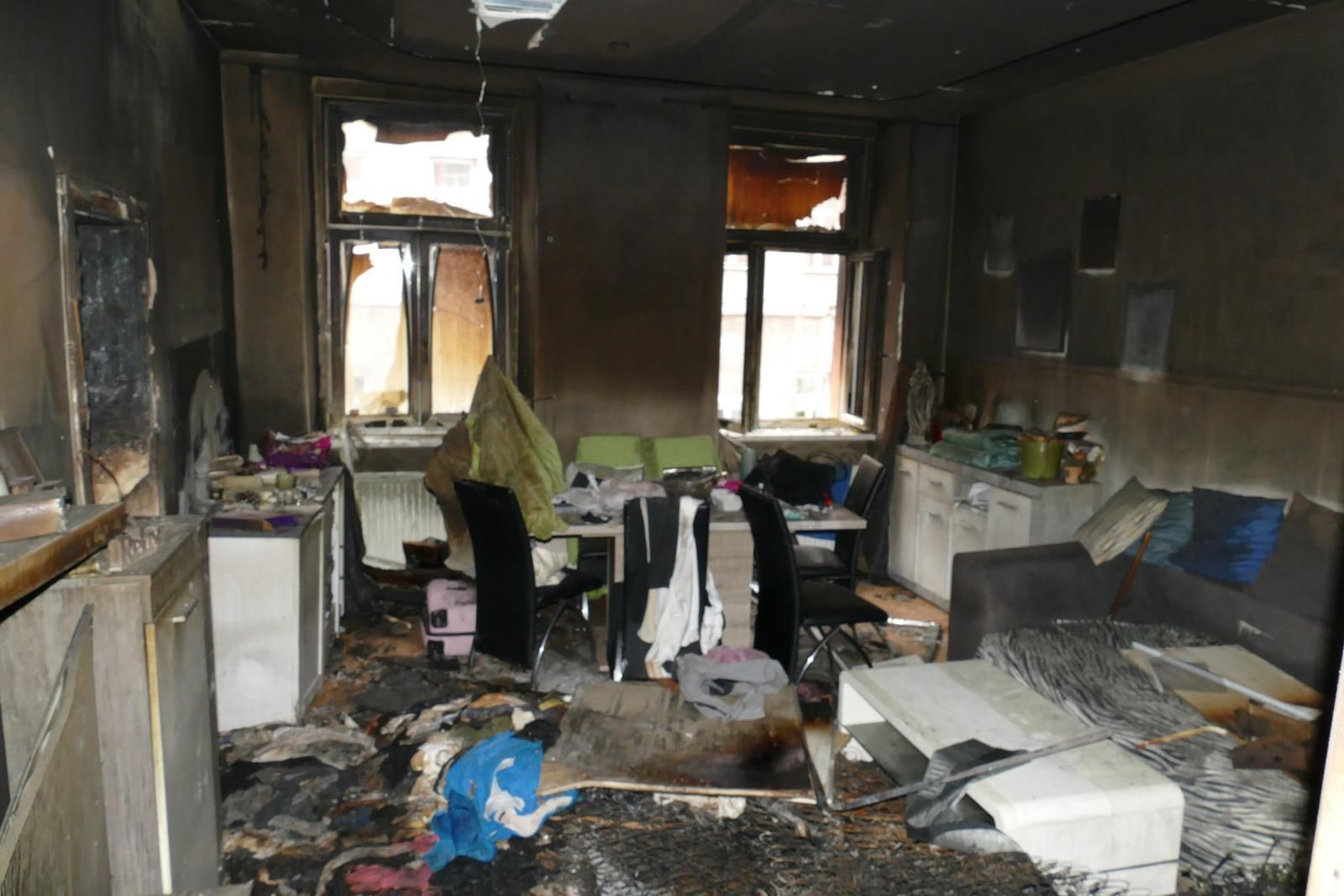 Ein Wohnzimmer mit verkohlten Wänden und Decke, das erhebliche Brandschäden aufweist, mit verstreuten, geschwärzten Trümmern.