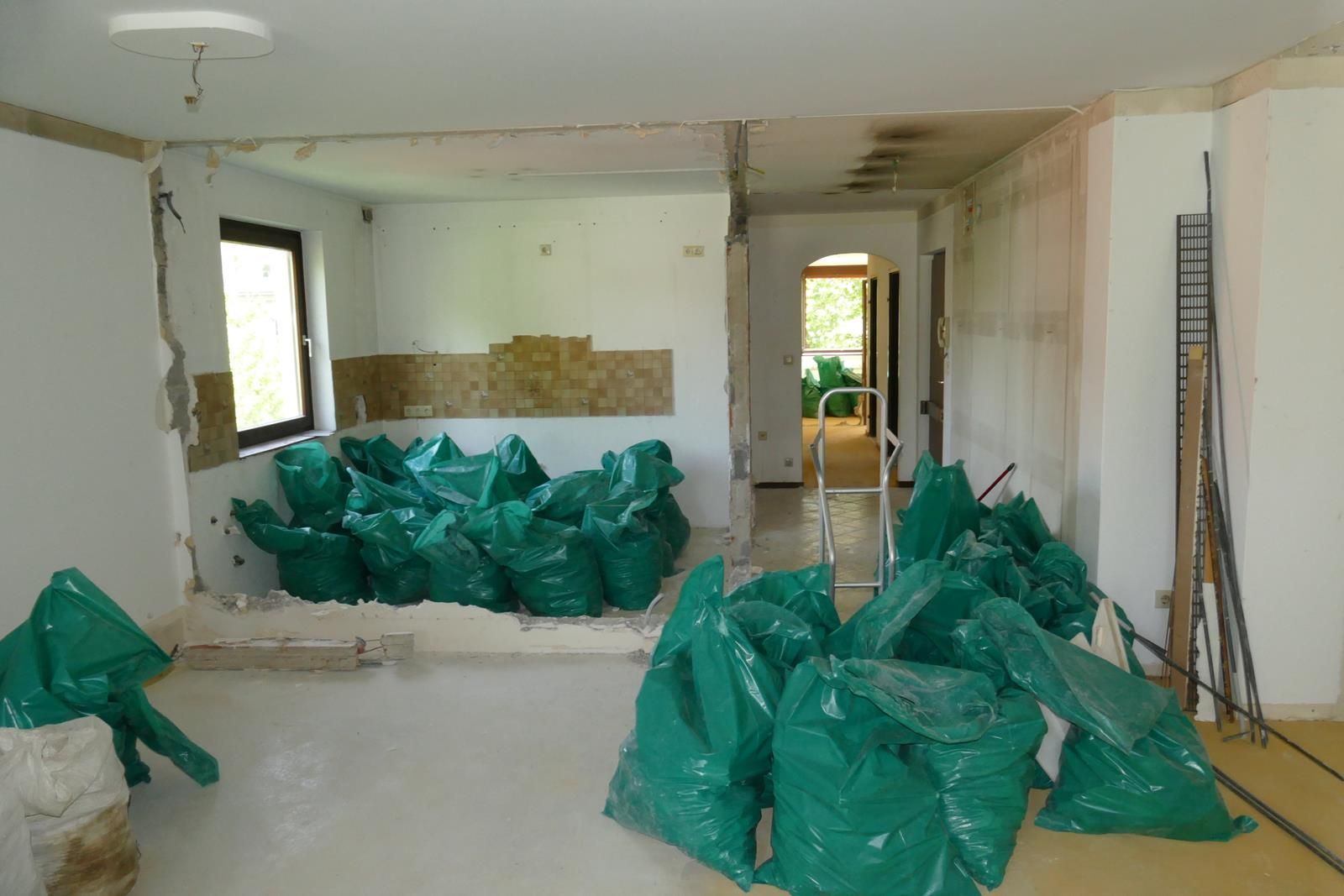 Ein Raum, der gerade renoviert wird, mit Bergen von grünen Bauschuttsäcken, die über den Boden verstreut sind, und offenen Wänden, die den Blick auf die Baustelle freigeben.