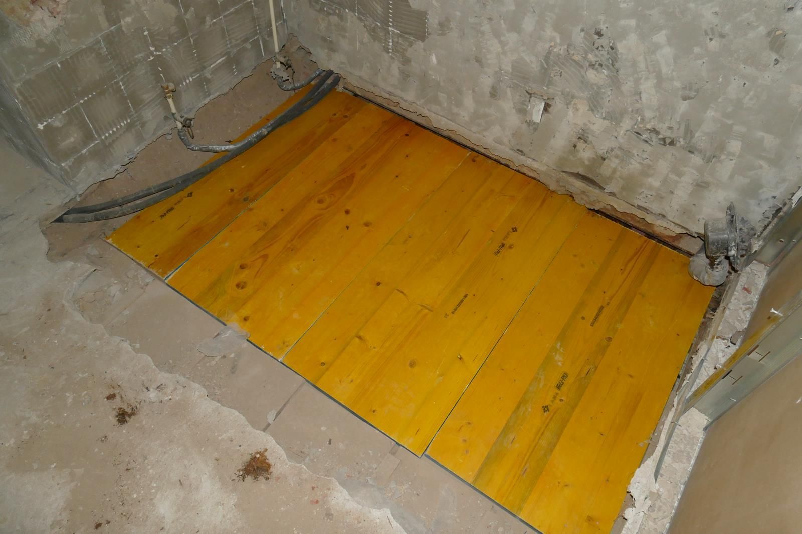 Ein Abschnitt gelber Holzdielen, die auf einem blanken Betonboden in einem im Bau befindlichen Raum verlegt sind.