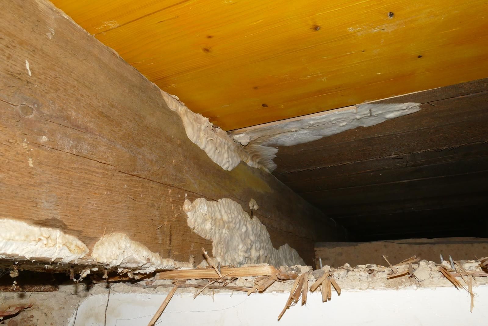 Expansionsschaum-Dichtstoff füllt die Spalten zwischen einem Holzbalken und einem Bodenbelag in einem Kriechkeller oder einer Kellerdecke.