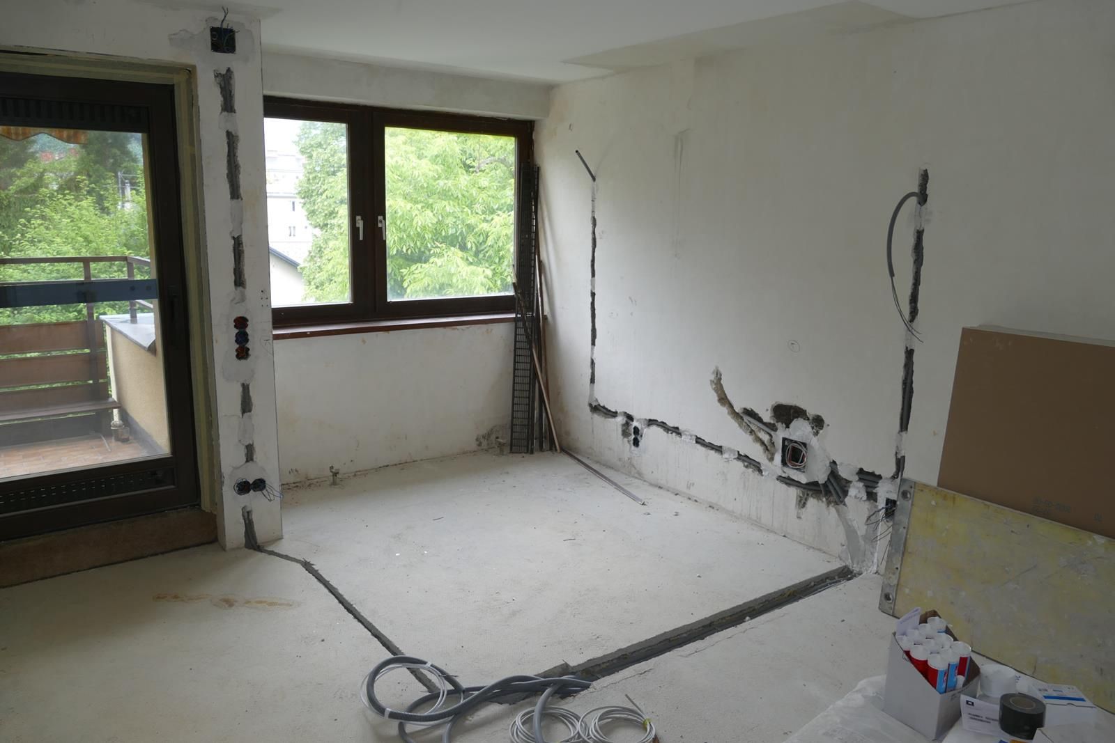Ein Raum, der gerade renoviert wird, mit freiliegenden elektrischen Leitungen, die in die weißen Wände und den Boden eingelassen sind.