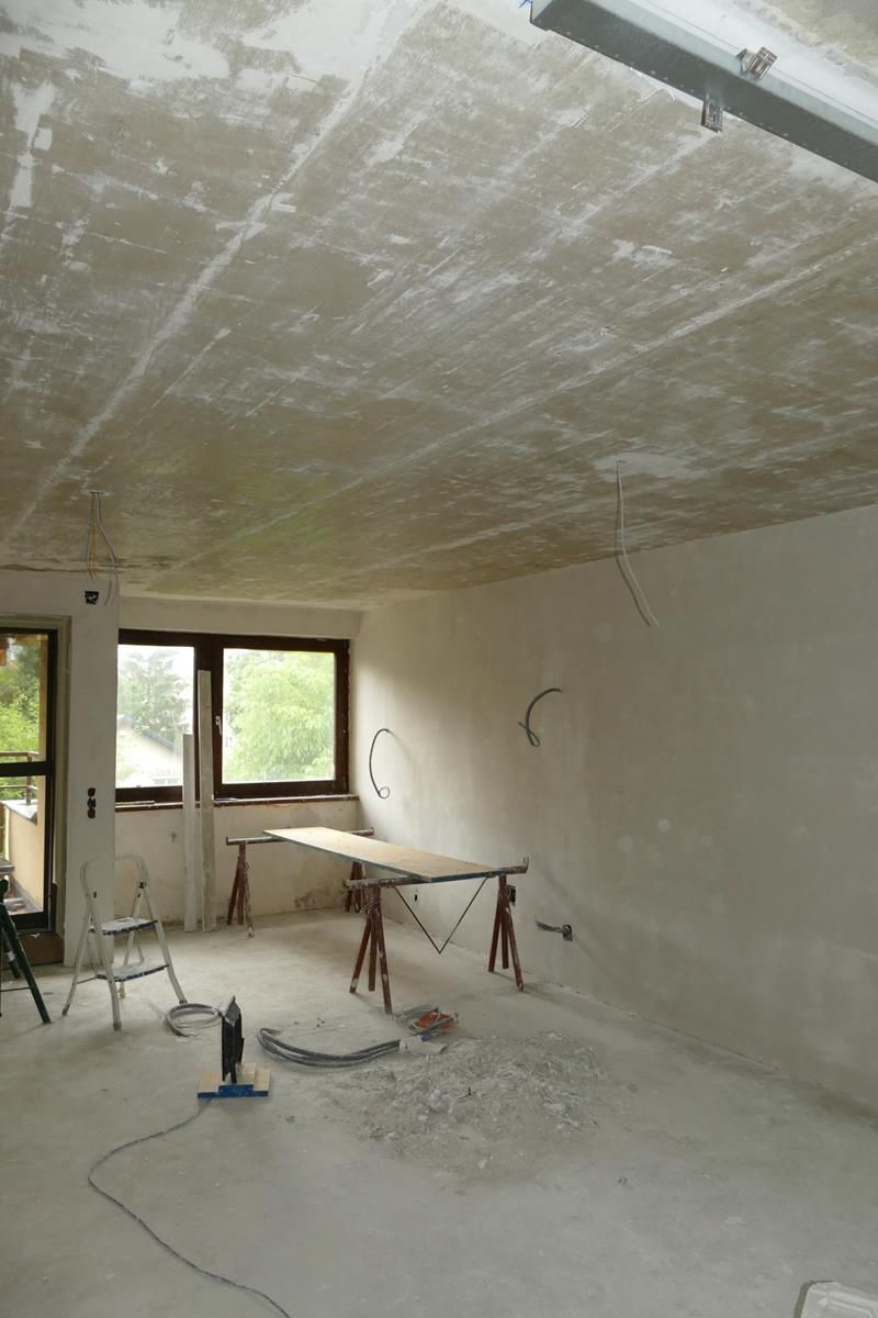 Ein unfertiger Raum, der renoviert wird: Die Wände sind verputzt, die Decke wird vorbereitet und in der Mitte befindet sich eine Werkbank.