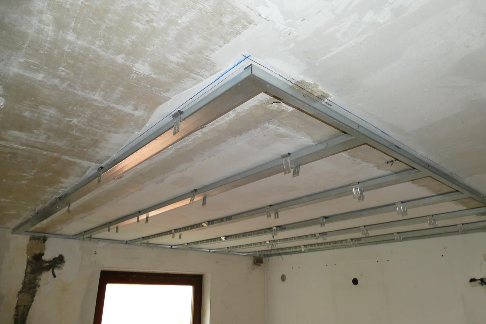 In einem Raum, der gerade renoviert wird, wird ein Metallgittergerüst für eine abgehängte Decke an einer Betondecke montiert.