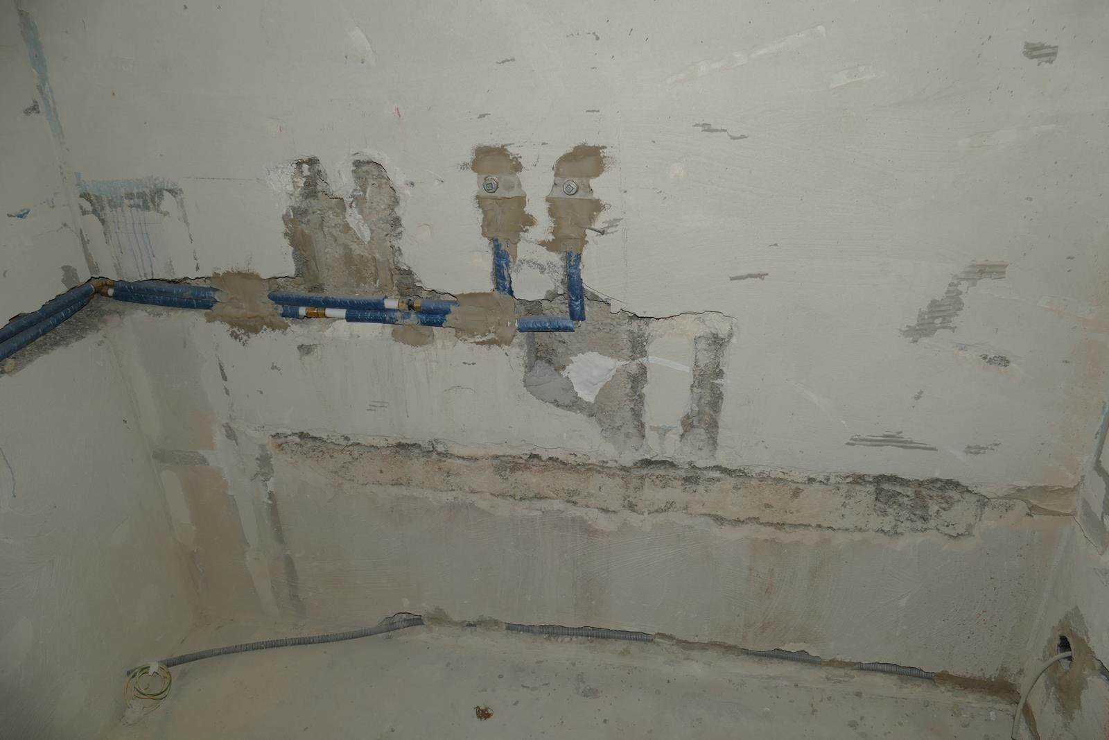 Eine unfertige Innenwand mit freiliegenden blauen Wasserleitungen, die in Putzstellen eingebettet sind und auf den endgültigen Wandputz warten.