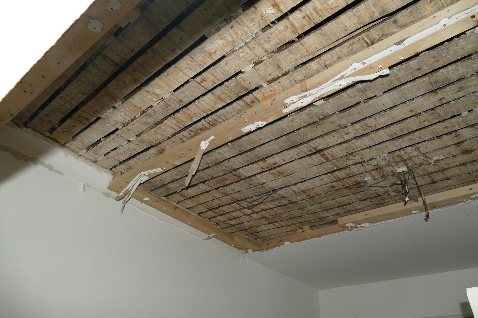 Ein Blick ins Innere zeigt eine beschädigte Decke, von der der Putz abgeplatzt ist und die Holzlatten und die tragenden Balken freilegt.