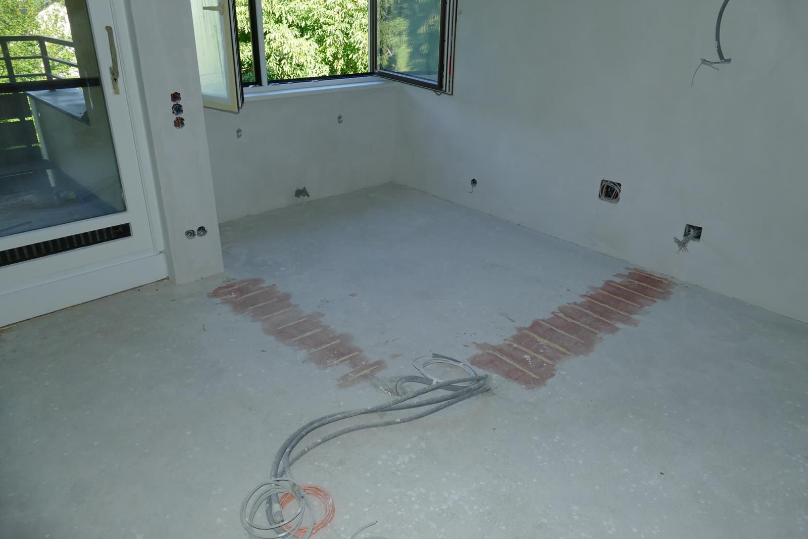 Ein unfertiger Raum mit hellgrauem Betonboden, auf dem zwei rechteckige Flächen aus rötlich-braunem Füllmaterial zu sehen sind.