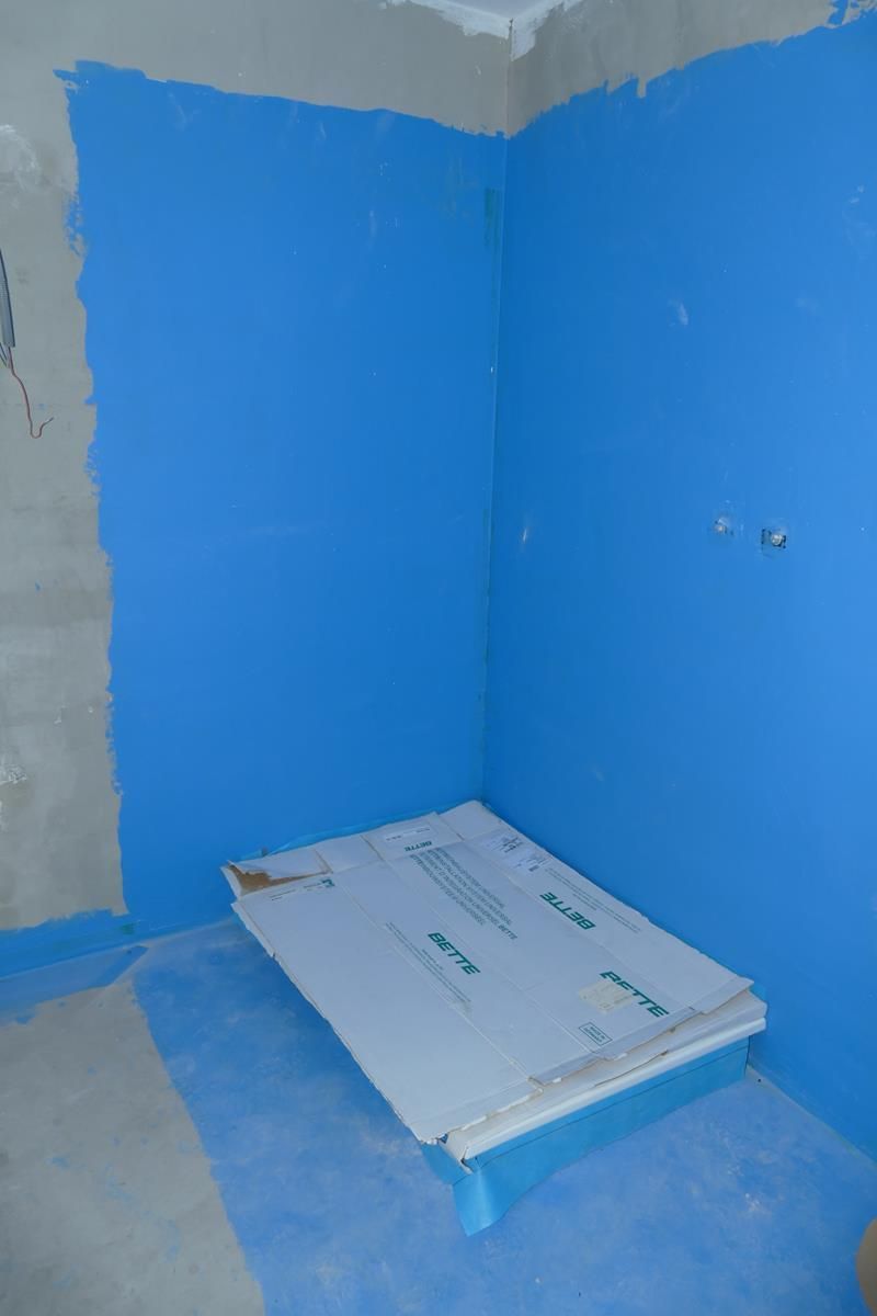 Eine Duschecke mit blauer, wasserdichter Membran an Wänden und Boden, die über eine abgedeckte Duschwanne verfügt.