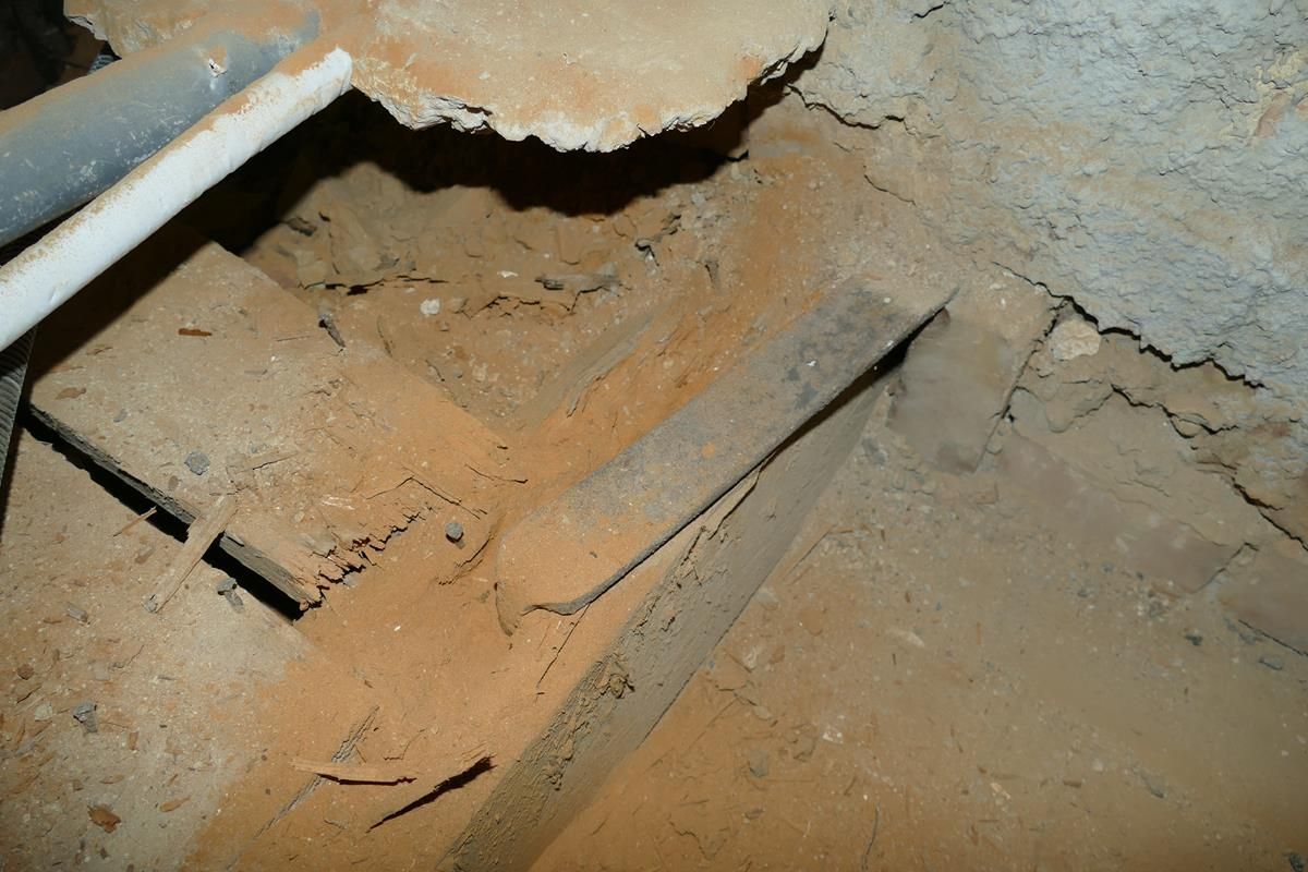 Eine Nahaufnahme von hölzernen Tragkonstruktionen, die mit Holzresten bedeckt sind, im Inneren eines Kriechkellers oder unterhalb eines Gebäudes.