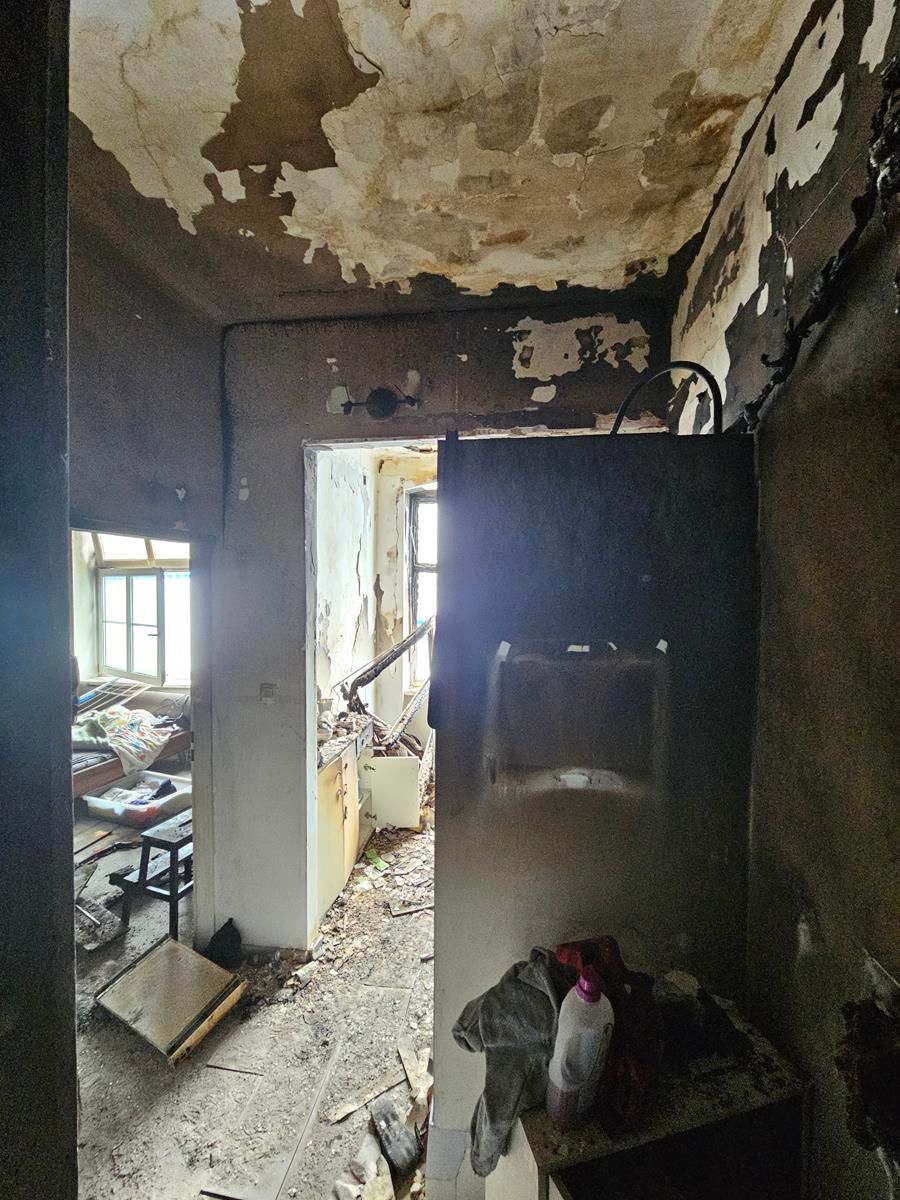 Der Blick durch eine Türöffnung in einen heruntergekommenen Raum mit abblätternder Farbe, Schutt auf dem Boden und einer dunklen, versengten Wand.