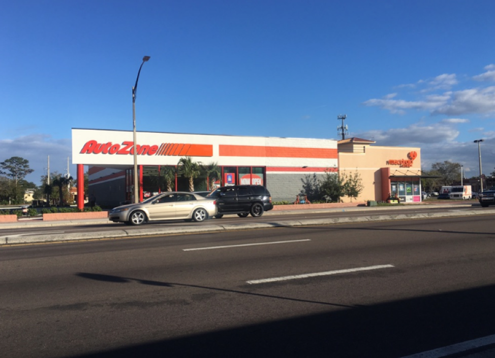 AutoZone store exterior on a sunny day, with parked cars and a clear blue sky.
