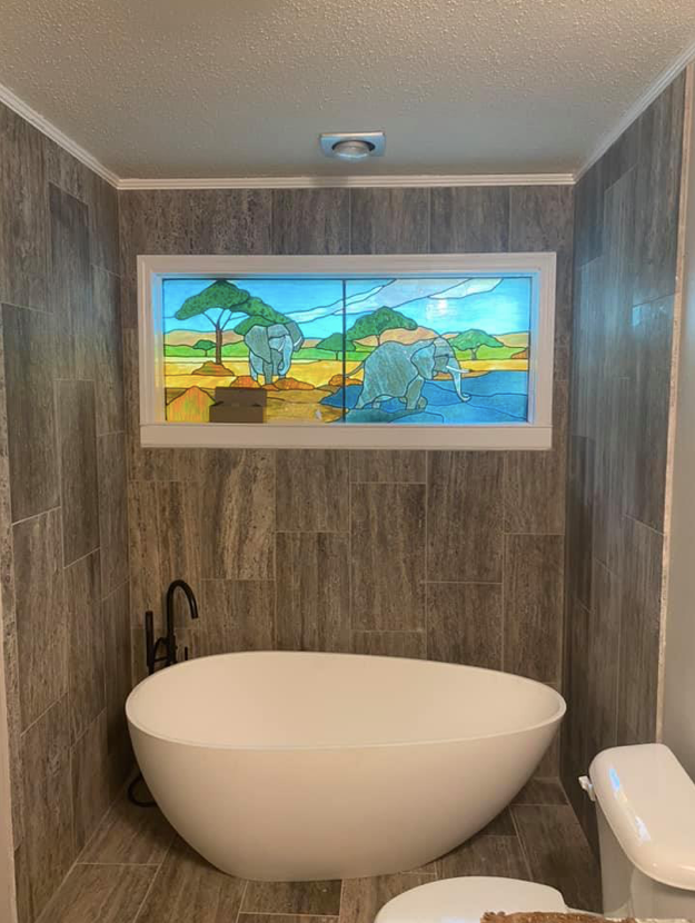 Modern bathroom with a freestanding tub, toilet, and colorful framed landscape artwork above the tub