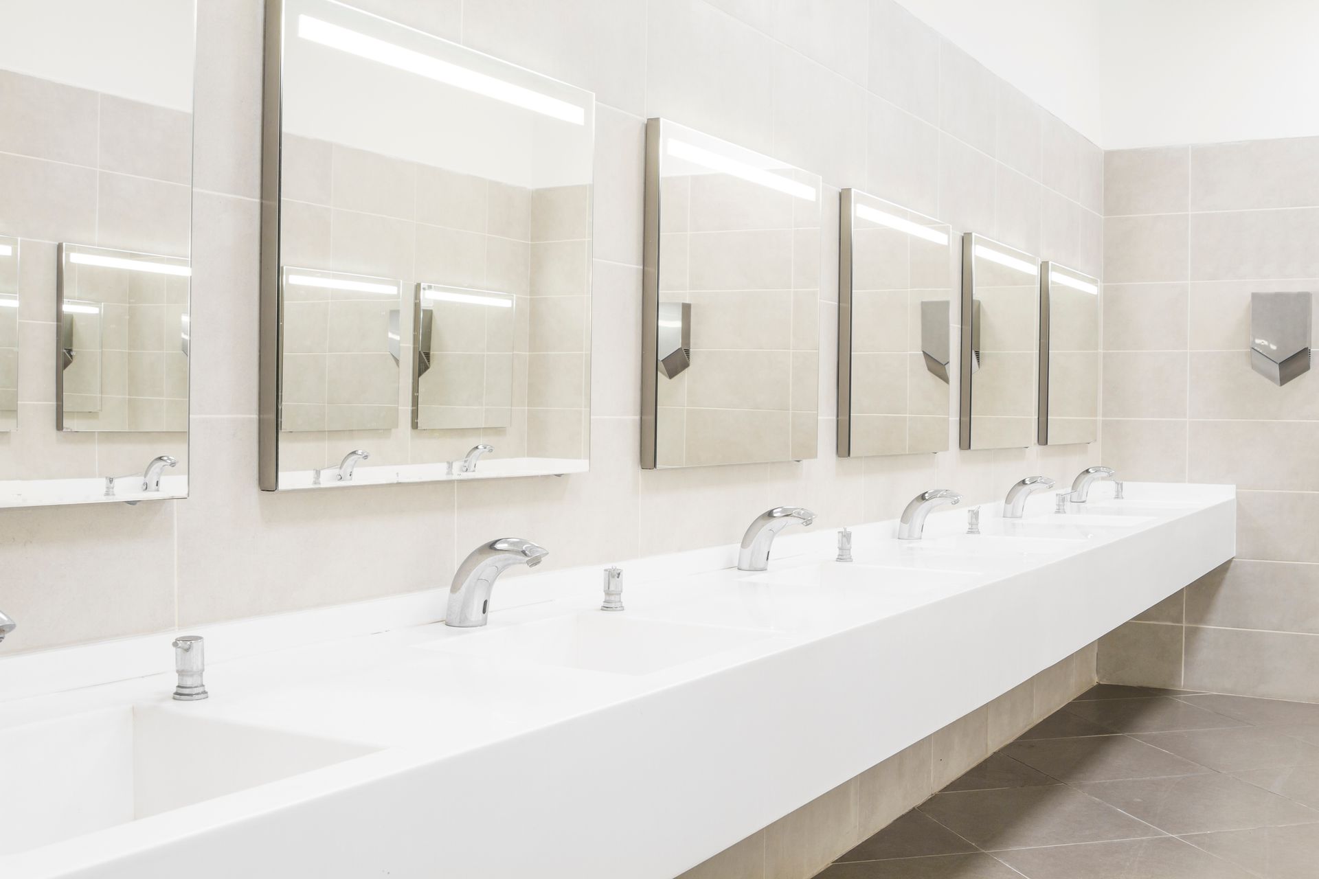 Bright restroom with a long white sink counter and mirrors above the faucets.