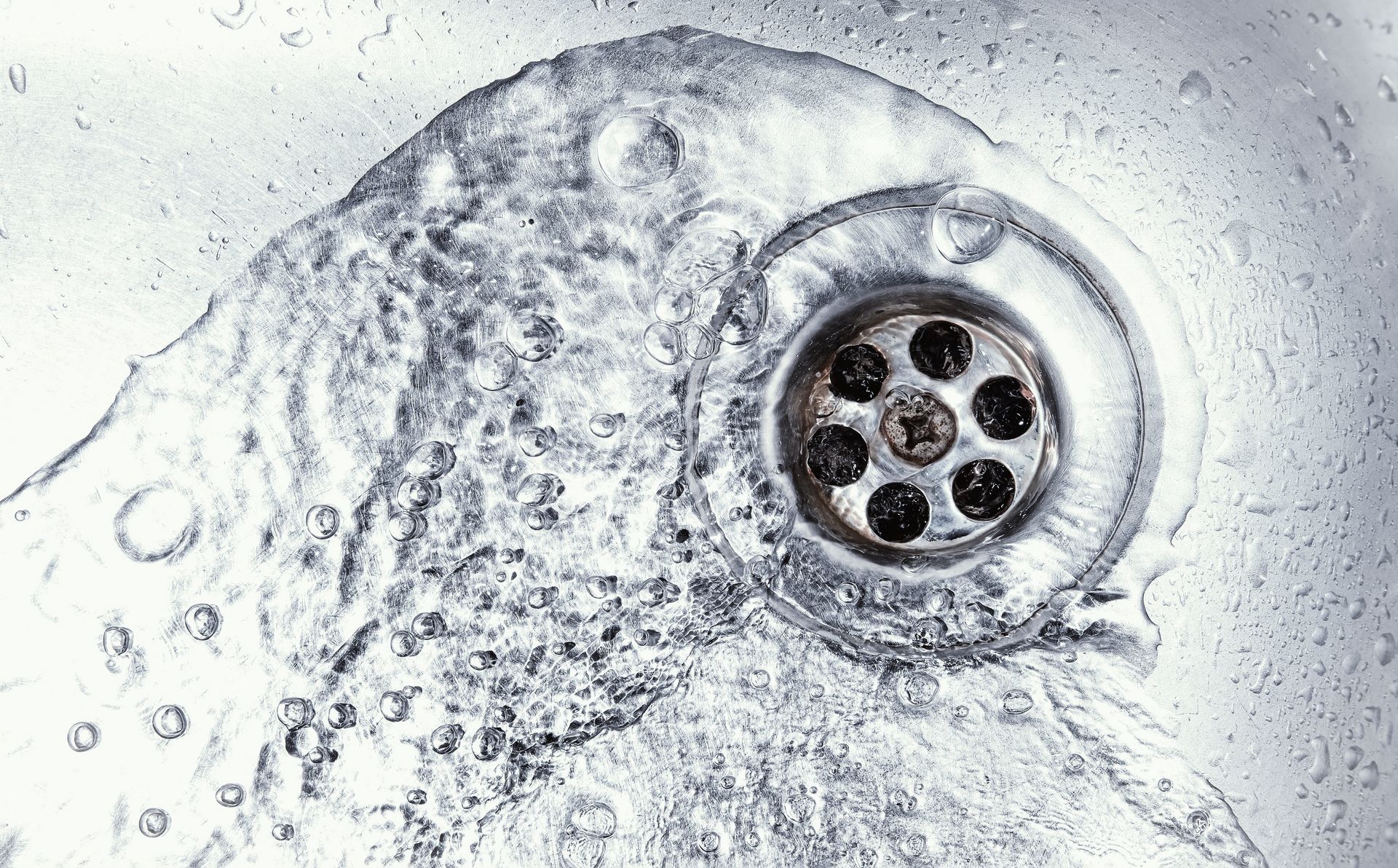 Close-up of a silver metal drain with a circular strainer in a white sink or basin
