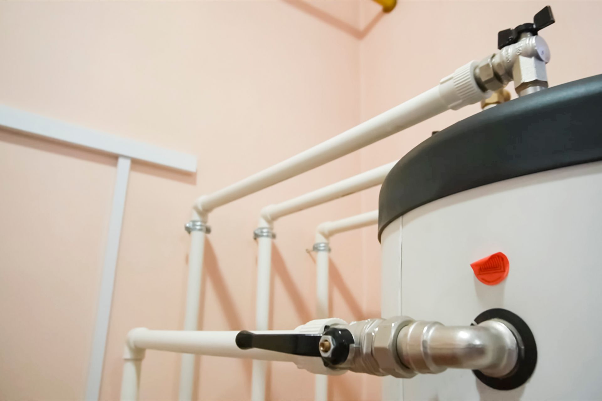 White plumbing pipes and valves connected to a large gray tank in a utility room