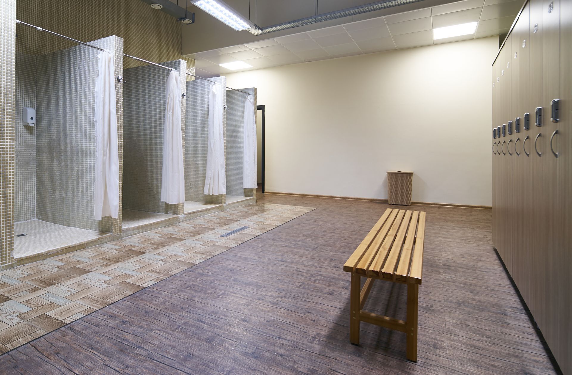 Locker room with showers, benches, and tiled flooring under bright fluorescent lights