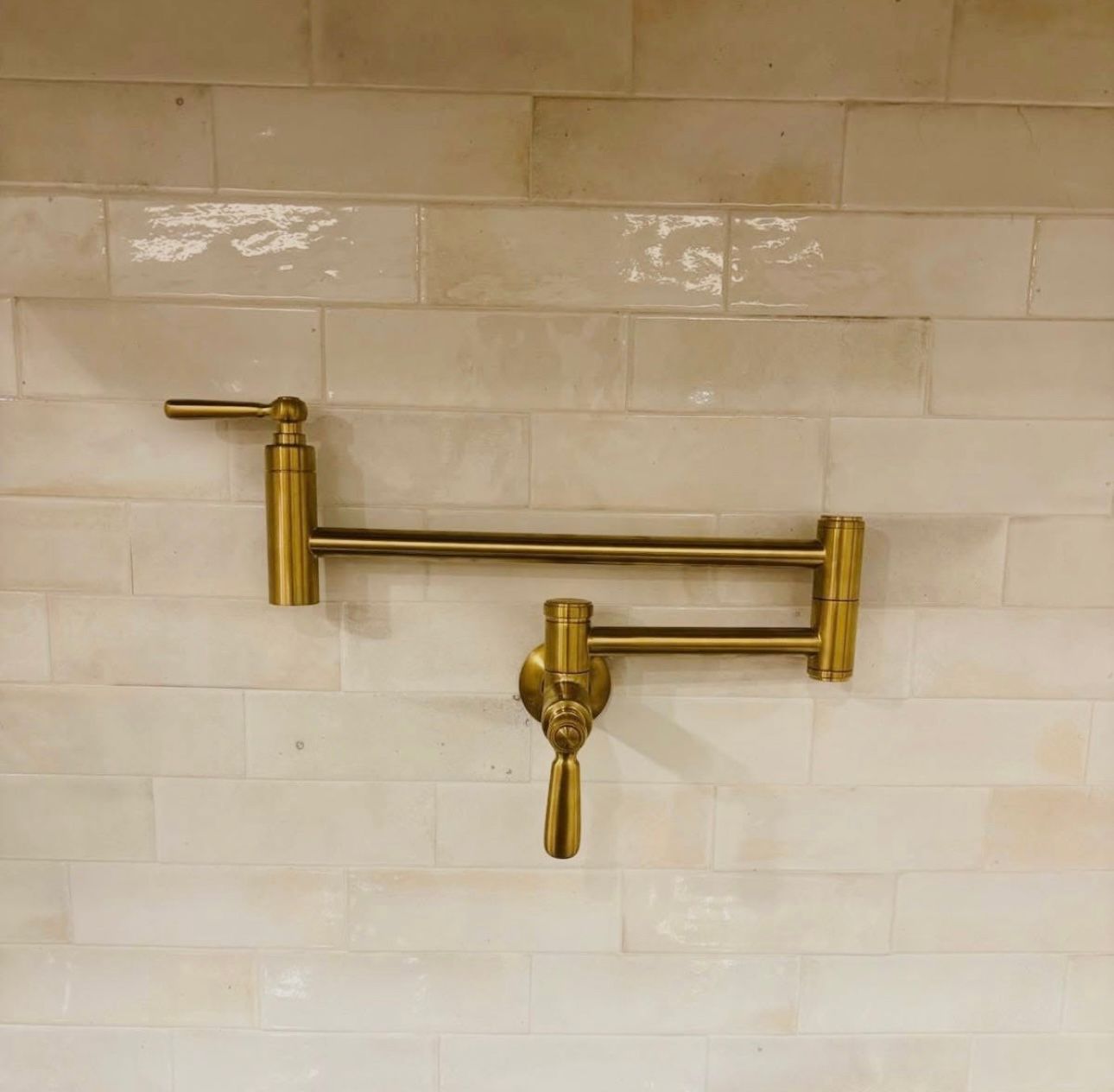 White kitchen stove with brass knobs under a brass pot-filler on a hex tile backsplash