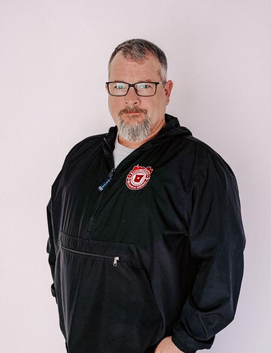 Man in a black hoodie with glasses, standing against a plain white background.