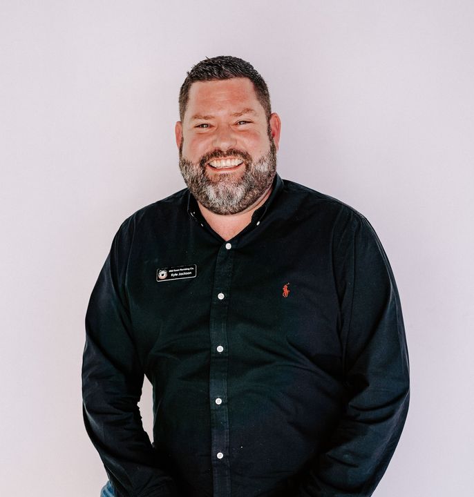 Smiling man in a black button-up shirt standing against a light gray background