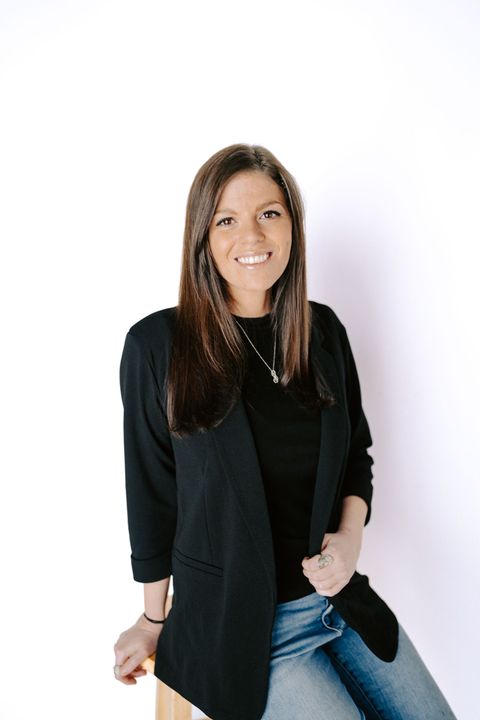 Woman in black cardigan and jeans smiling against a white background