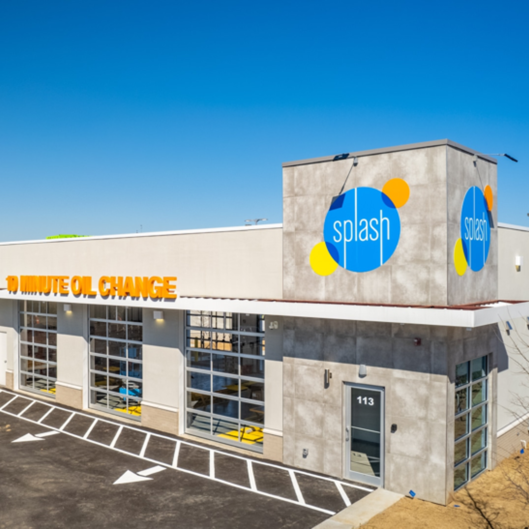 Exterior of a Splash car wash building with white and gray walls, blue signage, and orange lettering under a clear sky