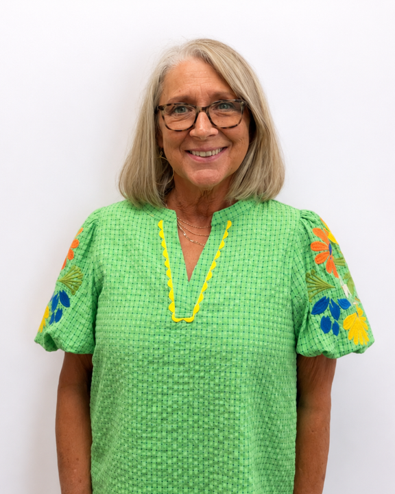 Smiling woman in green patterned blouse with yellow trim against a white background
