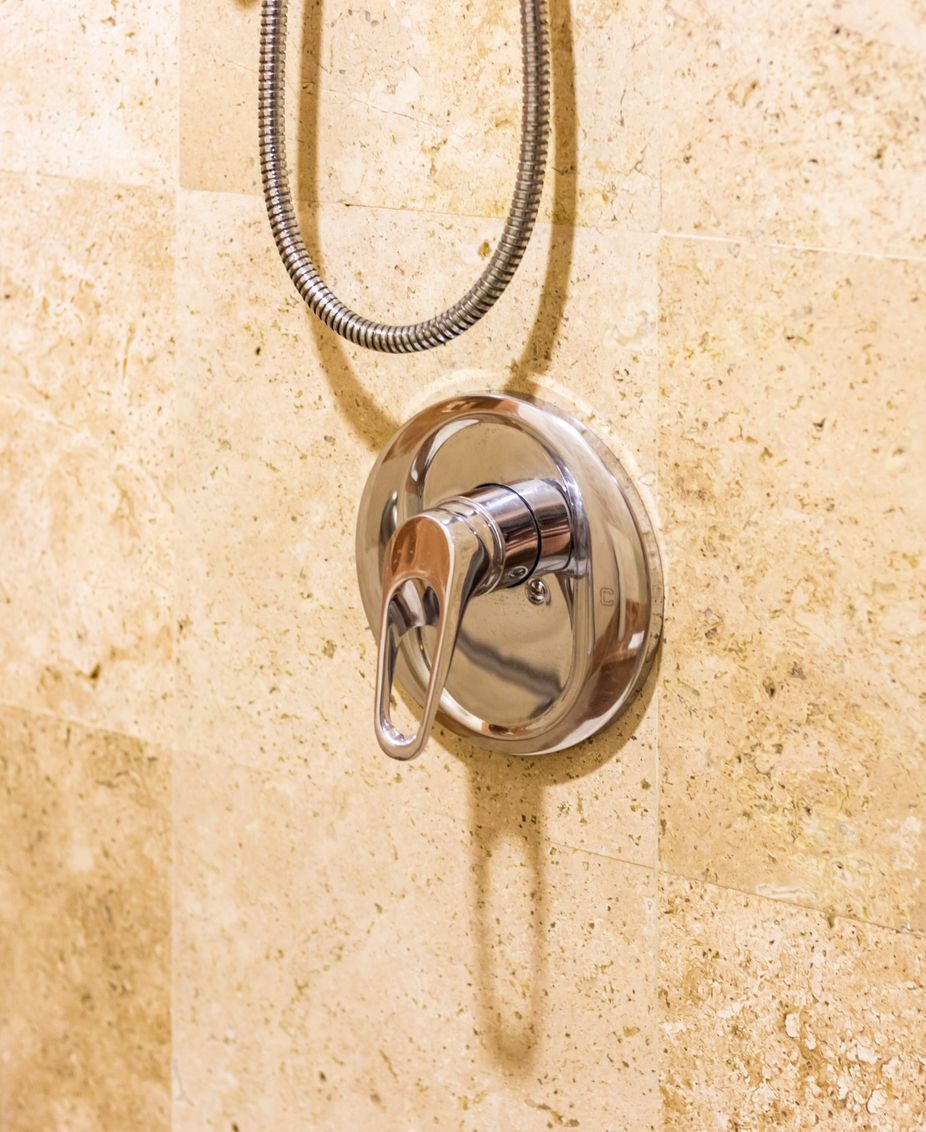 Chrome shower faucet with hanging hose on beige tiled wall