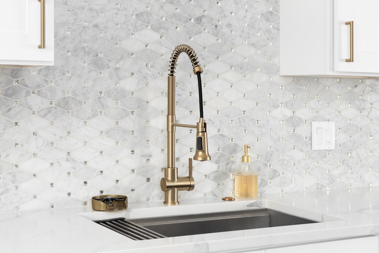Modern kitchen sink with gold faucet, white marble backsplash, and built-in soap dispenser