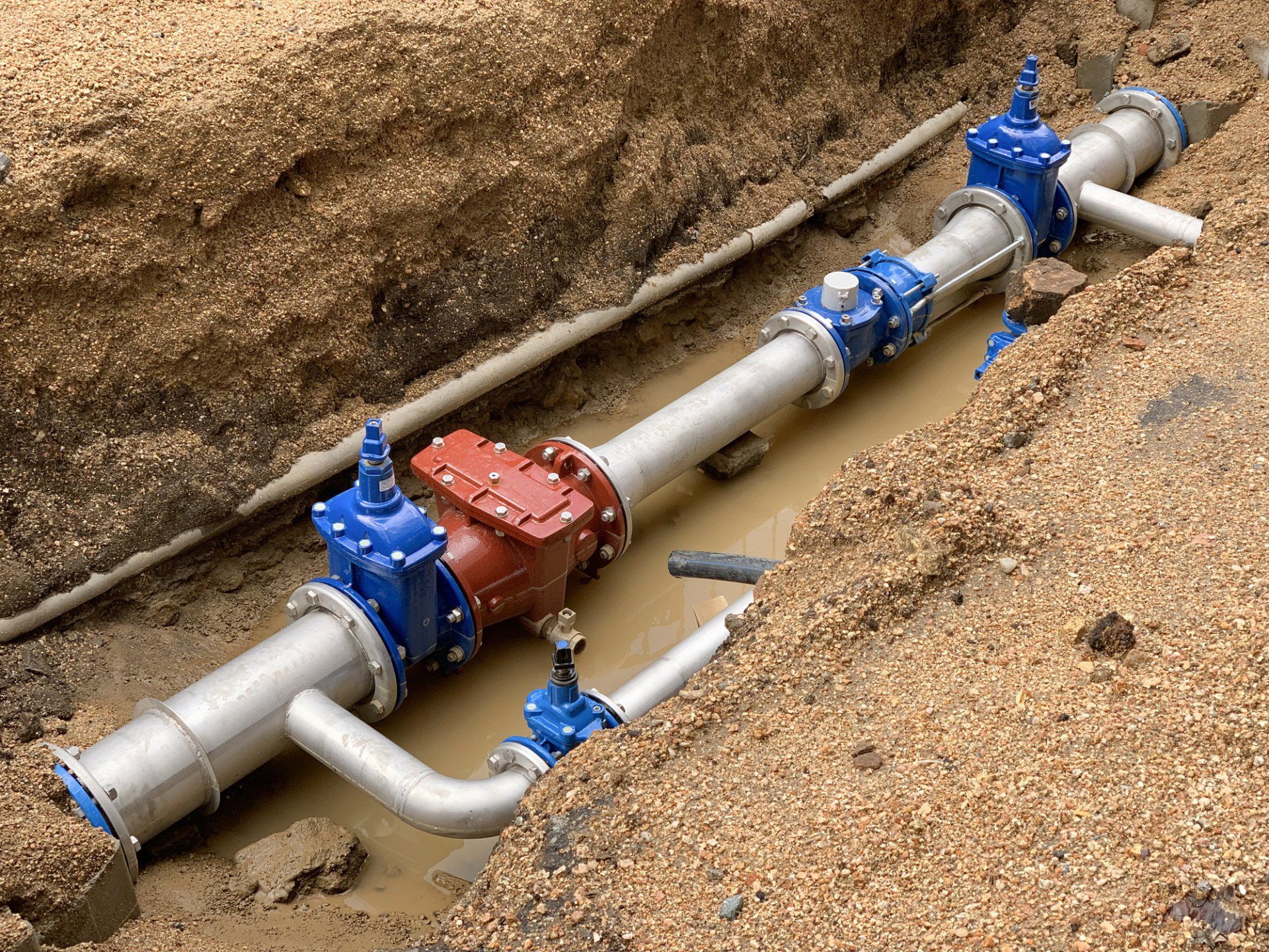Underground water pipeline with blue valves and a red control unit in an excavated trench
