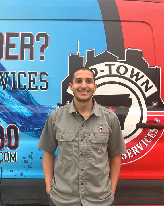 Smiling person standing in front of a red-and-blue service van with the Hometown Services logo