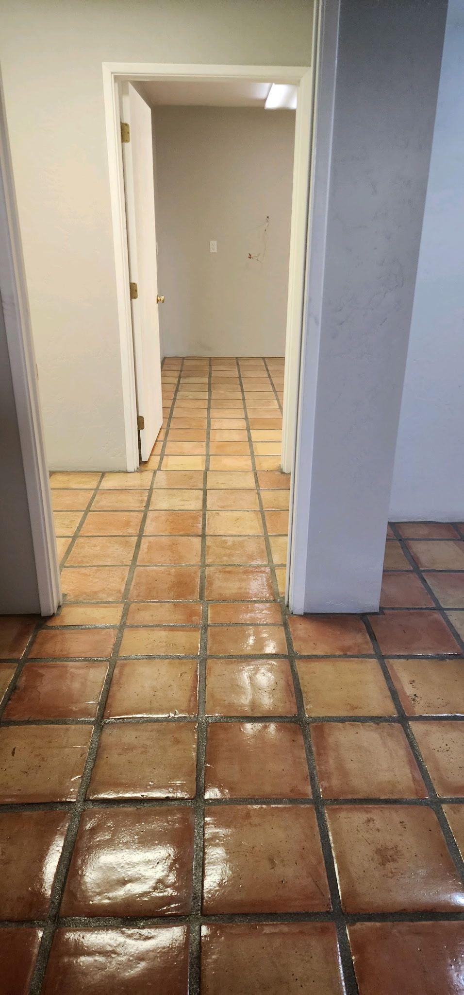 A hallway with tile floors and a door leading to a room.