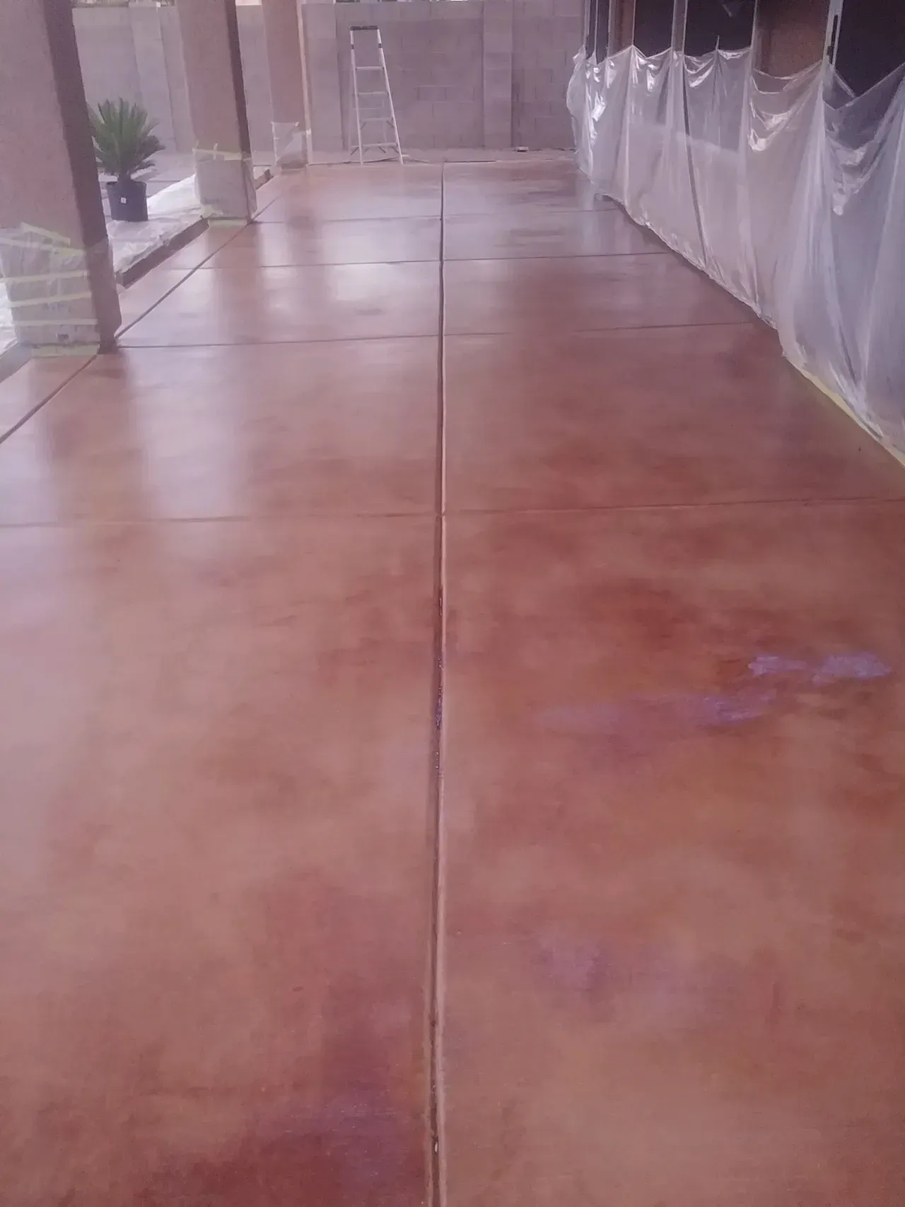 A concrete floor is being painted in a room with a ladder.