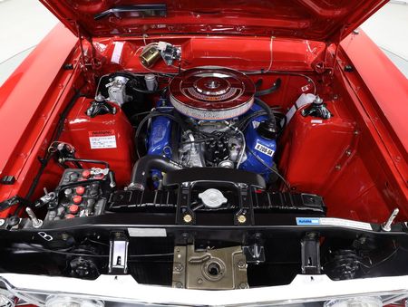 The engine of a red car is shown with the hood open.