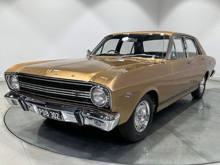 A gold ford falcon is parked on a turntable in a showroom.