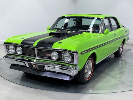 A green car with black stripes on the hood is parked on a glass display.