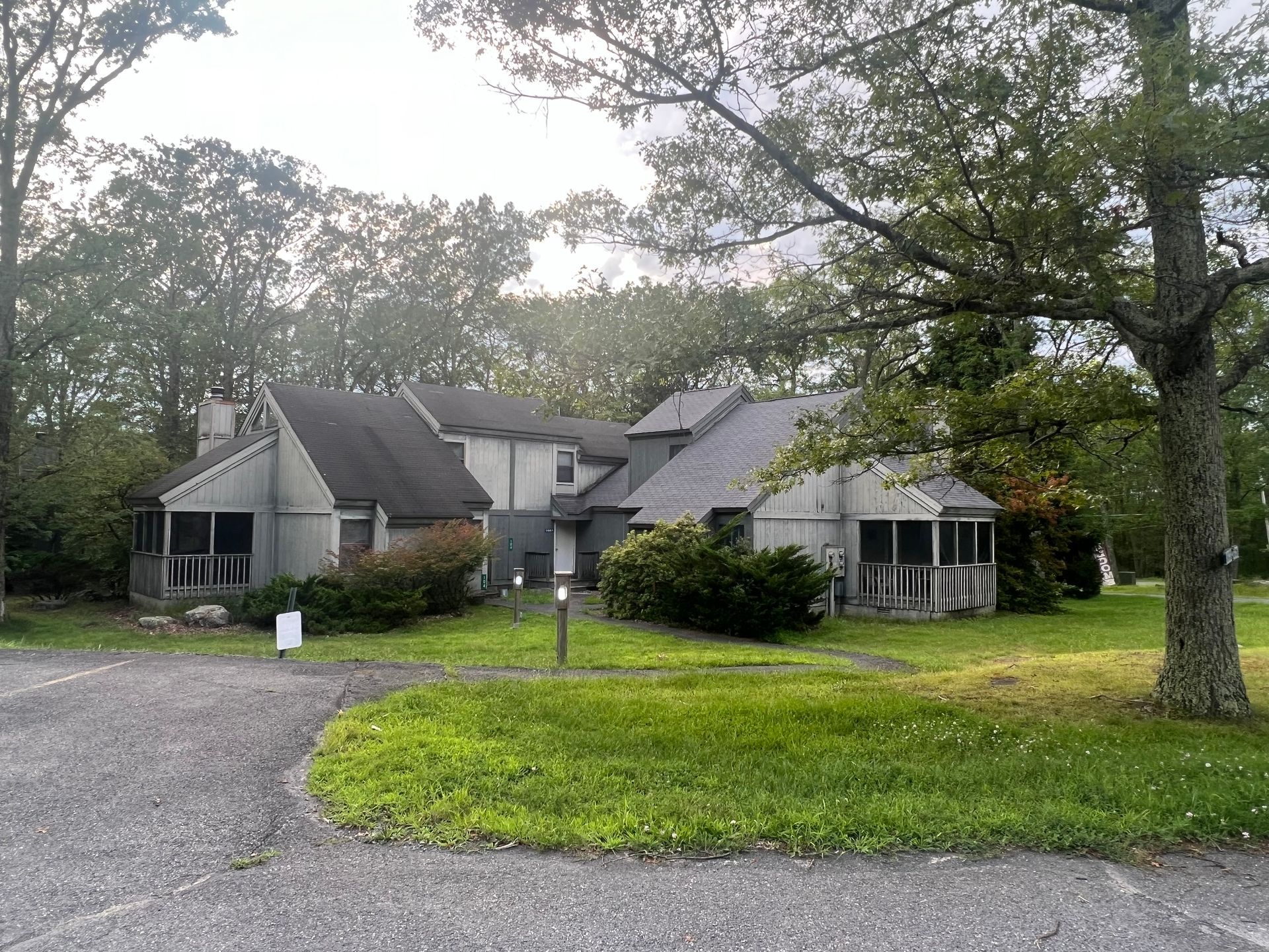 A large house with a screened in porch is surrounded by trees and grass.
