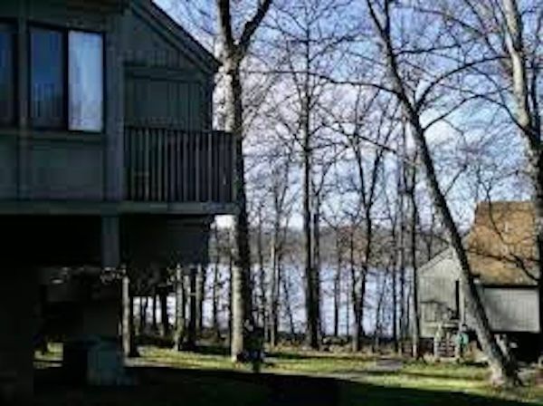 A house with a balcony overlooking a lake surrounded by trees.