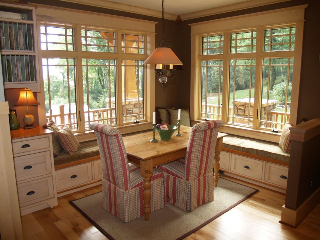 Sunlit dining nook with wooden table, striped chairs, bay windows, and built-in benches in a cozy room