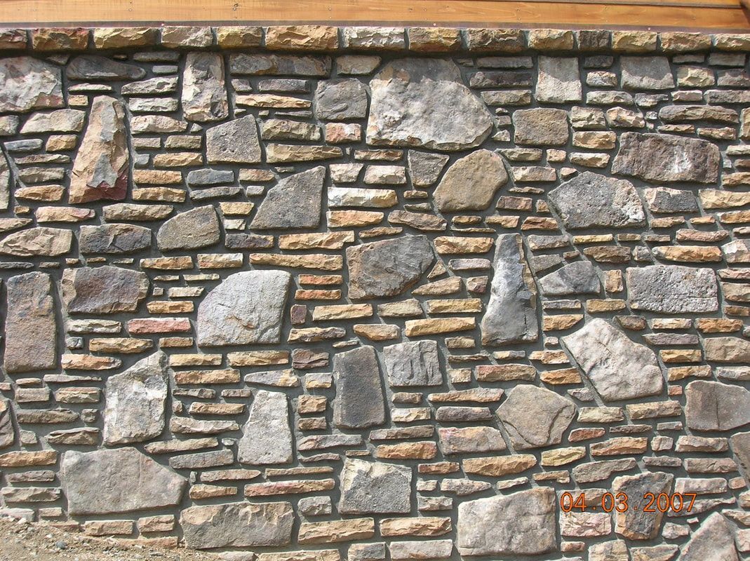 Stone wall made of gray and tan rocks with a wooden trim at the top