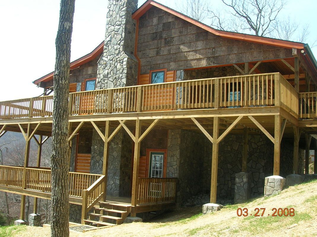 Rustic wooden cabin with large deck and stone chimney in a wooded setting